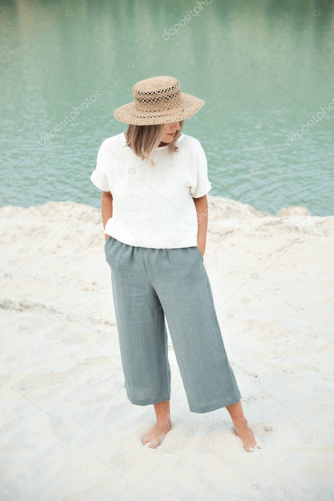 Stylish girl in linen clothes and straw hat. Relaxing in beach, simple slow life style