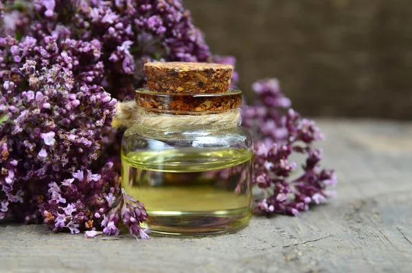 Oregano essential oil in a glass bottle with fresh blooming herb twigs on a wooden background.Aromatherapy, natural cosmetics,spa or bodycare concept.Selective focus.