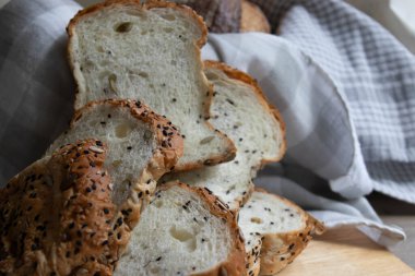Tahta bir yüzeye düzgünce dizilmiş taze çoklu tahıllı ekmek dilimleri, kısmen yumuşak kareli kumaşa sarılmış..