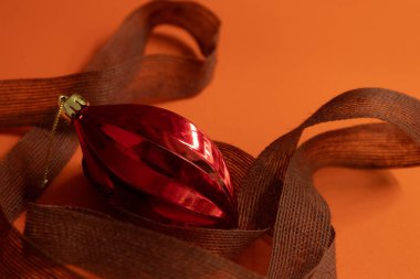 Kırmızı parlak takı, turuncu arka planda kahverengi kurdele.