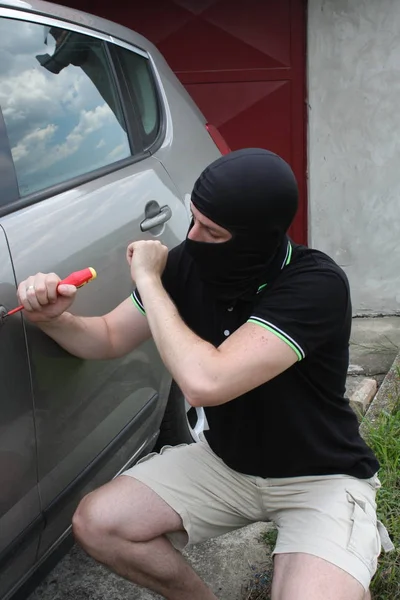 Car thief trying to break into a car with a screwdriver.