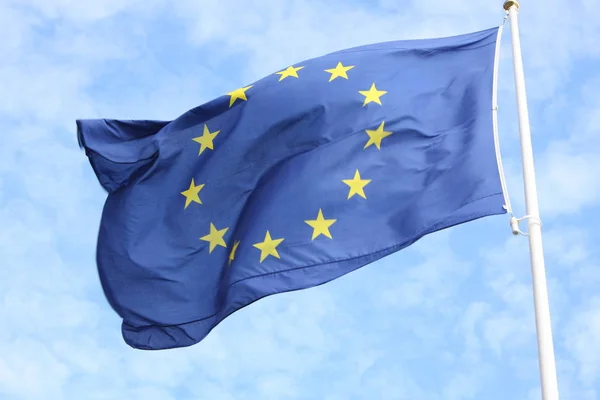 Closeup of single european flag with twelve yellow stars waving in the wind in front of blue sky