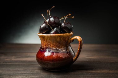 Olgun tatlı kiraz meyveleri damla bir ahşap yüzeyde bir kahverengi hamurlu tabak içinde.