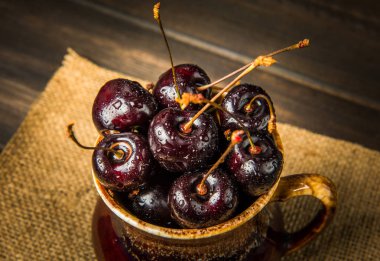 Olgun tatlı kiraz meyveleri damla bir ahşap yüzeyde bir kahverengi hamurlu tabak içinde.