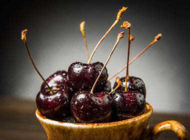 Olgun tatlı kiraz meyveleri damla bir ahşap yüzeyde bir kahverengi hamurlu tabak içinde.