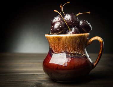 Olgun tatlı kiraz meyveleri damla bir ahşap yüzeyde bir kahverengi hamurlu tabak içinde.