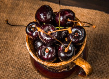 Olgun tatlı kiraz meyveleri damla bir ahşap yüzeyde bir kahverengi hamurlu tabak içinde.