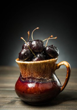 Olgun tatlı kiraz meyveleri damla bir ahşap yüzeyde bir kahverengi hamurlu tabak içinde.