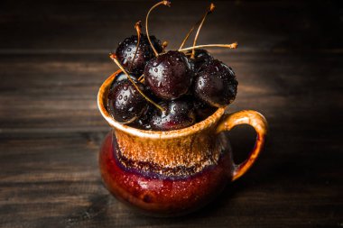Olgun tatlı kiraz meyveleri damla bir ahşap yüzeyde bir kahverengi hamurlu tabak içinde.