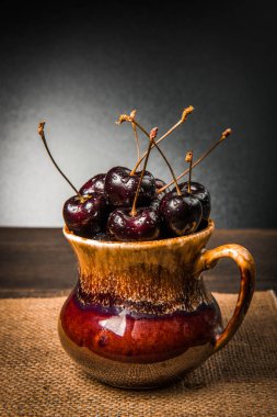 Olgun tatlı kiraz meyveleri damla bir ahşap yüzeyde bir kahverengi hamurlu tabak içinde.