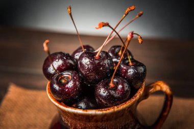 Olgun tatlı kiraz meyveleri damla bir ahşap yüzeyde bir kahverengi hamurlu tabak içinde.