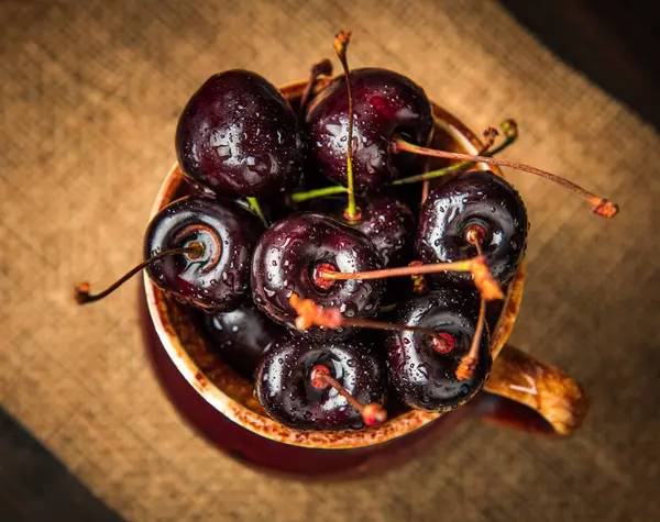 Olgun tatlı kiraz meyveleri damla bir ahşap yüzeyde bir kahverengi hamurlu tabak içinde.
