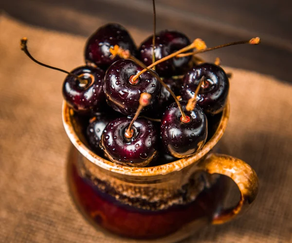 Olgun tatlı kiraz meyveleri damla bir ahşap yüzeyde bir kahverengi hamurlu tabak içinde.