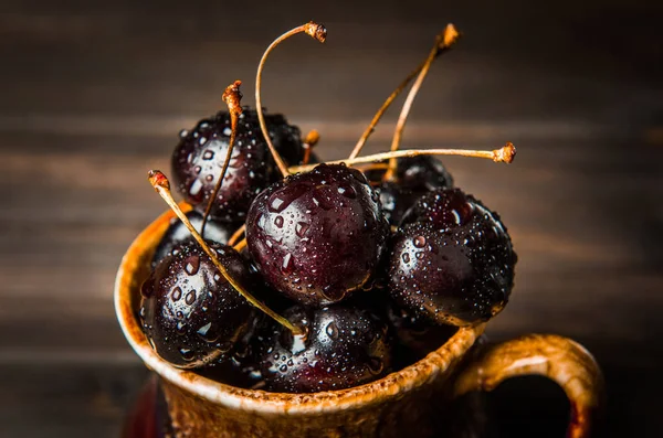 Olgun tatlı kiraz meyveleri damla bir ahşap yüzeyde bir kahverengi hamurlu tabak içinde.