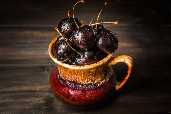 Olgun tatlı kiraz meyveleri damla bir ahşap yüzeyde bir kahverengi hamurlu tabak içinde.