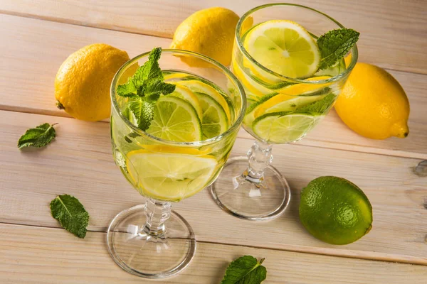 Yaz kokteyl mojito kireç ve ahşap zemin üzerine nane ile yenileniyor. Taze yaz yeşil yaprakları güzel gözlük narenciye ve güzel kokulu içkiyle buzlu.