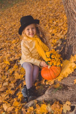 Sonbahar arka planda büyük kabak ile küçük güzel sarışın kız