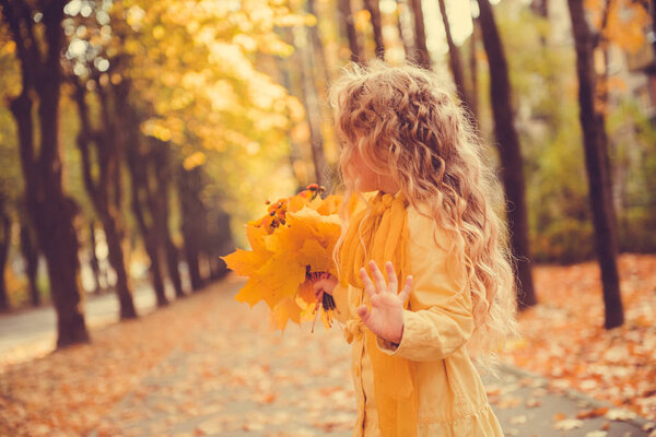 Little girl with blond hair in autumn background with flowers and suitcase