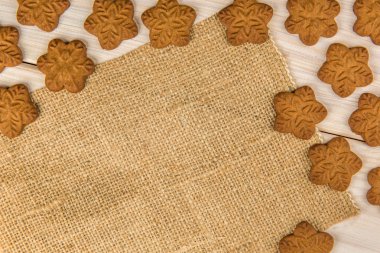 Noel ve yeni yıl gingerbread çerezleri kahverengi çuval arka plan dokusu üzerinde çerçeveli kar taneleri ile.