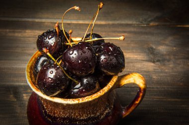 Olgun tatlı kiraz meyveleri damla bir ahşap yüzeyde bir kahverengi hamurlu tabak içinde.