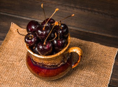 Olgun tatlı kiraz meyveleri damla bir ahşap yüzeyde bir kahverengi hamurlu tabak içinde.