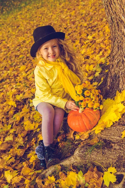 Küçük sarışın kız ve sonbahar arka planda büyük kabak.