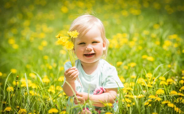 Hermosa niña feliz sentada en un prado verde con flores amarillas dientes de león —  Fotos de Stock