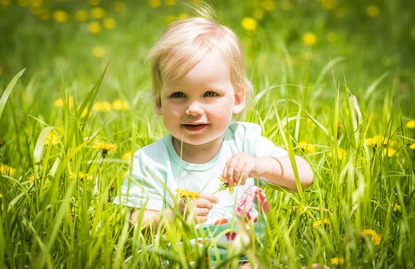 Belle petite fille heureuse assise sur une prairie verte avec des fleurs jaunes pissenlits — Photo