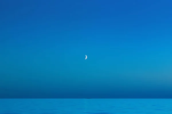 无云的海军蓝天 海面上挂着月牙 抽象模糊的背景美丽的夜间海景与复制空间 2020年流行色彩 经典蓝色 图库照片