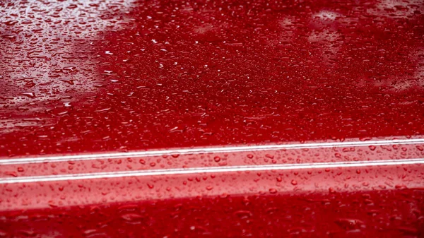 Yakalanmış damlacıklar pürüzsüz, kırmızı bir yüzeye tutunarak dokulu bir görünüm yaratıyorlar. Odak, su ve renk arasındaki etkileşimi vurgulayarak, doğal bir ortamda yavaşça yer değiştirir..