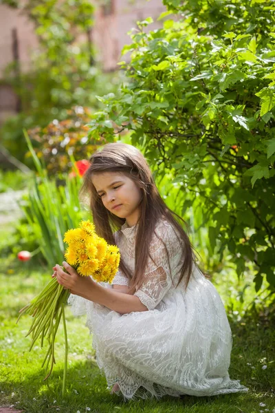 Güzel beyaz elbiseli şık bir kız yeşil yapraklı sarı karahindiba çiçekleriyle poz veriyor.