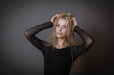 Siyah elbiseli genç bir kadın karanlık bir duvara karşı poz veriyor.