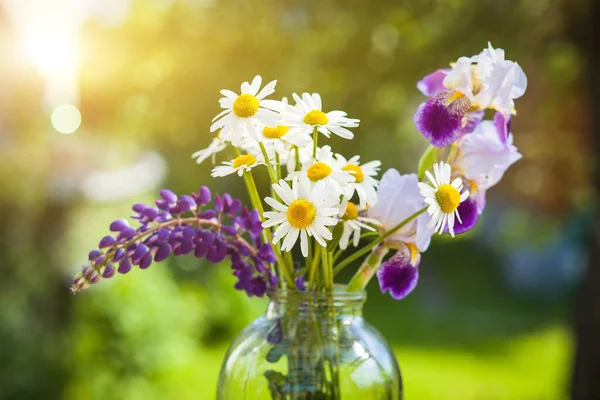 Beautiful bouquet of wild flowers in the light of the setting sun in a glass vase