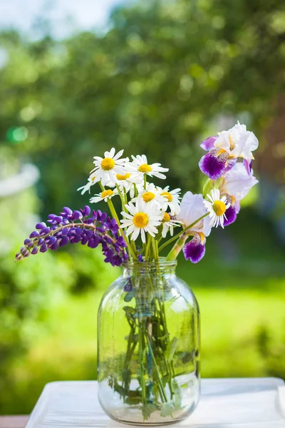 Beautiful bouquet of wild flowers in the light of the setting sun in a glass vase