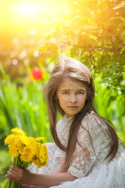 Hafif elbiseli şık bir kız poz verir ve büyük bir buket sarı karahindiba tutar.
