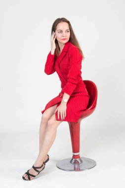 Kırmızı takım elbiseli güzel bir genç kadın kırmızı bir sandalyede oturuyor.