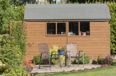 A Dutch style wooden garden shed with patio and two chairs clipart