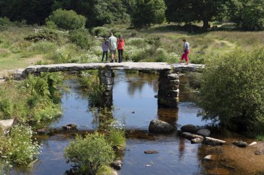 Turist Postbridge, Dartmoor Milli Parkı, Devon, İngiltere Doğu Dart Nehri üzerinde Antik clapper köprünün diğer tarafında yürümek