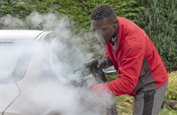 Man steam cleaning a luxury car on a home visiting valet service, England UK