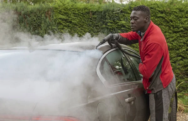 Man steam cleaning a luxury car on a home visiting valet service, England UK