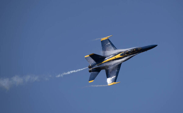 Military jet showing smoke and condensation against a blue sky