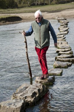 Ogmore Vale of Glamorgan Güney Galler İngiltere'de, nehir Ewenny üzerinde taşlar stepping arasında yürüyen yaşlı adam