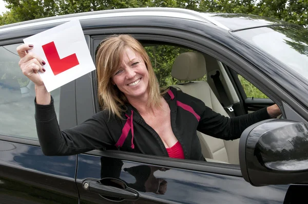 Mature female driver smiling & holding a learner L plate