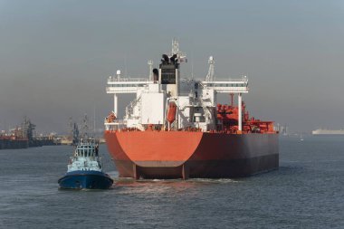Tug with a stern line attached manouvering a crude oil tanker ship onto a berth at a refinery clipart