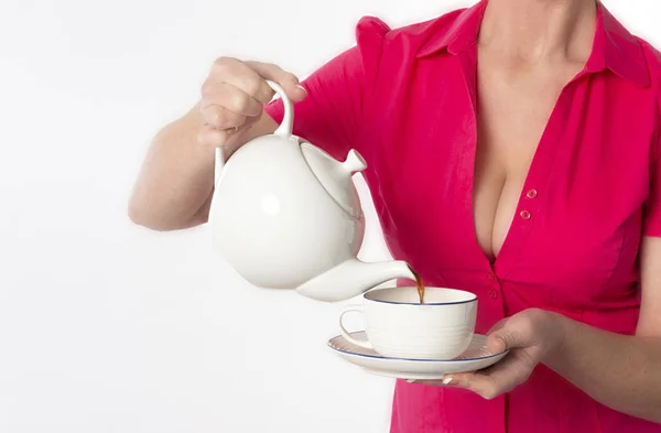 Southern England UK. circa 2018. Attractive woman wearing a revealing red shirt pouring a cup of tea