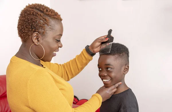 Nine year old boy with curly hair with his mother using a wide tooth afro comb for his hair. Andover, Hampshire, England, UK. April 2019.