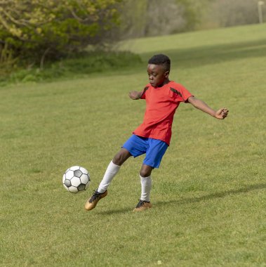 Hampshire, England, UK. April 2019. A nine year old footballer dribbles the soccer ball during a training session in a public park. clipart