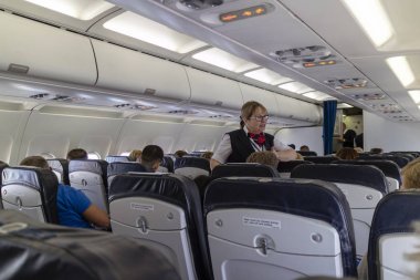 Mürettebat üyesi olan bir yolcu jetinde, bir A320 düzleminde kulüp sınıfında bir yolcuya konuşan bir uçak uçağı servisi. Circa 2019.