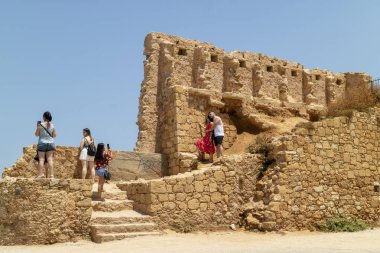 Chania, Girit, Yunanistan. Haziran 2019. Eski Venedik Limanı duvarında fotoğraflanan turistler, Hanya, Girit 'te mavi bir gökyüzüne karşı kalır..