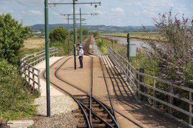Seaton, Devon, İngiltere, İngiltere. Haziran 2019. Riverside Depot'ta bir tramvay çalışanı Doğu Devon'daki Axe Nehri'nin yanında durur..